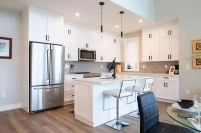 a kitchen with white cabinets and a stainless steel refrigerator at The Luna, New Penthouse w Patio, Lake and Mtn Views in Harrison Hot Springs
