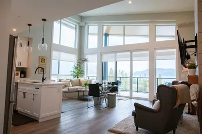 a kitchen and living room with a large window at The Luna, New Penthouse w Patio, Lake and Mtn Views in Harrison Hot Springs