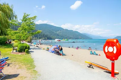 a beach with people on the sand and the water at Echo Beach, 2 Bed, Lake View and Walkable to Beach in Harrison Hot Springs