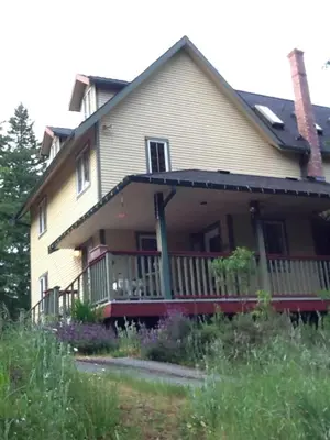 a large house with a porch with a fence at Wisteria Honeymoon Cottage in Sooke