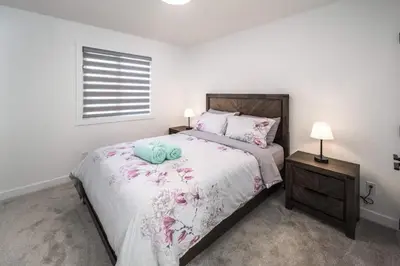 a white bedroom with a large bed with flowers on it at Near Downtown, Large 3BR! FREE Banff Pass in Calgary