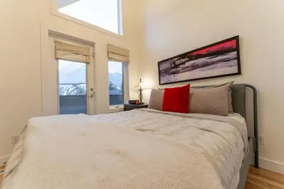 a bedroom with a large white bed and two windows at Alpine Village Condo by Canadian Rockies Vacation Rentals in Canmore