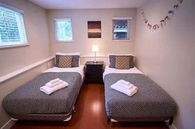 two twin beds in a small room with windows at Awesome 2BR in Lynn Valley in North Vancouver