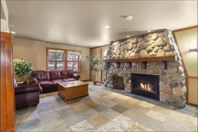 a living room with a large stone fireplace at Main Village, Ski-in Ski-out, Hot Tub, Condo in Sun Peaks