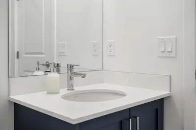 a white bathroom with a sink and a mirror at Skyline Retreat Spacious 4BR Home with Balcony! in Calgary