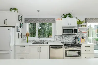 a kitchen with white cabinets and a sink and a stove at Bayview Bed and Breakfast in Mill Bay
