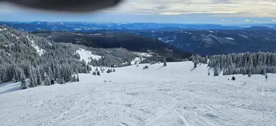 a snow covered slope with people skiing down a mountain at The Marmot's Den in Sun Peaks