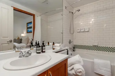 a bathroom with a sink and a tub and a mirror at Village Penthouse w Views Pool and Hot Tub in Whistler