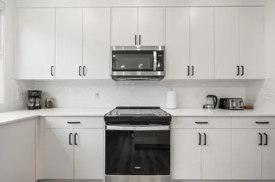 a kitchen with white cabinets and a microwave at Luxury 3 Bedrooms Spacious Townhome, 2 Car Garage, Sleeps 8, Heater & AC, King Bed, Easy Ski Access, Next to WinSport, 10km from Calgary Downtown, Near Banff in Calgary