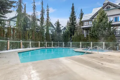 a swimming pool in front of a house with a fence at Whistler Village Condo Sleeps 7 in Whistler