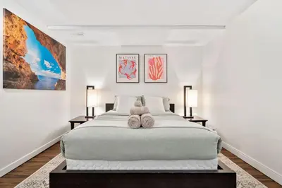 a white bedroom with a large bed with two lamps at 1 Bedroom Cozy Retreat - Queen Bed, Pet Friendly, Smart TV, Secure & Private Access, Free Parking, Netflix & More! in Calgary