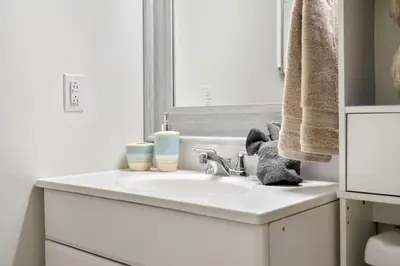 a white bathroom with a sink and a mirror at 1 Bedroom Cozy Retreat - Queen Bed, Pet Friendly, Smart TV, Secure & Private Access, Free Parking, Netflix & More! in Calgary