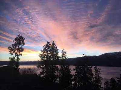a sunset over a lake with trees in the foreground at Desert Pines Holiday Getaway in Peachland