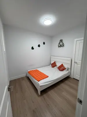 a small bedroom with a bed with an orange blanket at Sweet home 2 bedroom suite in Surrey