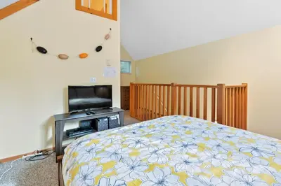 a bedroom with a bed and a flat screen tv at Tyee Retreat Cozy Lofted 1 Bedroom Cabin in Ucluelet