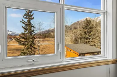 a window with a view of a house and mountains at Charming & Cozy 1-Bedroom Retreat in Canmore