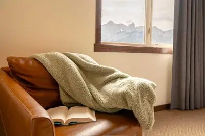a blanket sitting on a couch with a book at Breathtaking Luxury 3Bd Penthouse Pool and Hot Tub in Canmore
