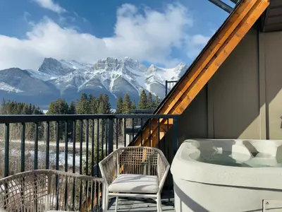 a balcony with a tub and chairs and mountains at Memory Lodge in Canmore