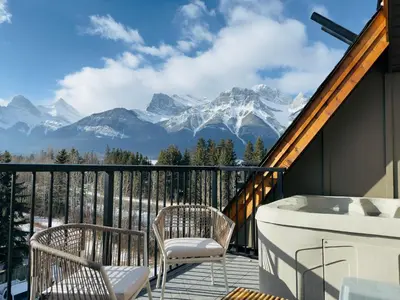 a balcony with a tub and chairs and mountains at Memory Lodge in Canmore