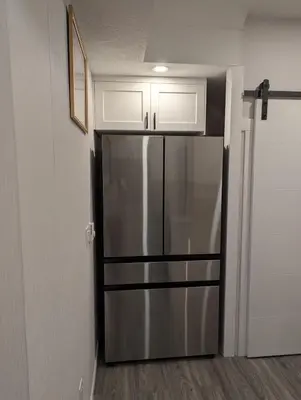 a stainless steel refrigerator in a kitchen with white cabinets at MIAT Apartment in Calgary
