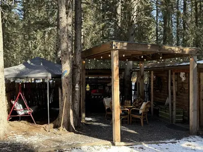 a wooden pavilion with a table and chairs in the woods at Rustic Cozy Cabin with hot tub in Bragg Creek