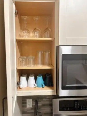 a kitchen cabinet with glasses and a microwave at Modern 3BR Near Airport & DT in Calgary