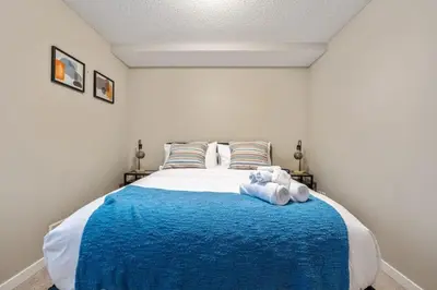 a bedroom with a large bed with a blue blanket at The Grande 1BD 1BA - Full Kitchen Guest Suite in Calgary