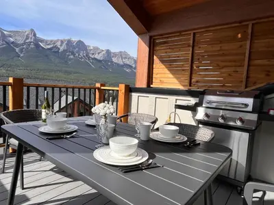 a table with plates and cups on a balcony with mountains at Top FL 2BR 2BA Hot Tubs phenomenal mountain views in Canmore