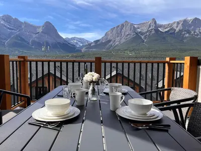 a table with plates and bowls on a balcony with mountains at Top FL 2BR 2BA Hot Tubs phenomenal mountain views in Canmore