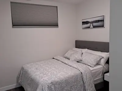 a white bedroom with a bed with a window at Cozy 2 Bedroom Walkout Basement in Calgary