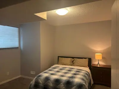 a bedroom with a bed and a lamp and a window at Spacious 2BR Suite - SW Edmonton in Edmonton