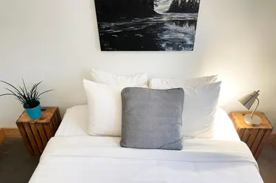 a bed with white sheets and a gray pillow on it at Tidal Retreat Cabin in Tofino