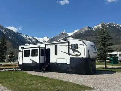 an rv parked in a field with mountains in the background at Fernie RV Resort in Fernie