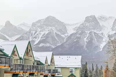 a group of buildings with snow covered mountains in the background at Scenic 2BR Haven with MTN Views Near DT Banff in Canmore