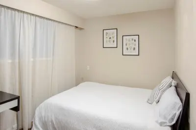 a white bedroom with a bed and a window at Convenient Urban Retreat in Vancouver