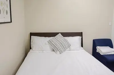 a bed with white sheets and pillows and a blue chair at Convenient Urban Retreat in Vancouver