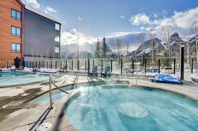 a hot tub in front of a building with snow covered mountains at 3 Bedroom with Heated Outdoor Pool and Hottub! in Canmore