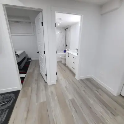 a bathroom with white walls and a wooden floor at Carrington Cozy Suite, Calgary in Calgary