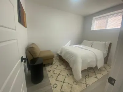 a bedroom with a bed and a chair and a window at Carrington Cozy Suite, Calgary in Calgary