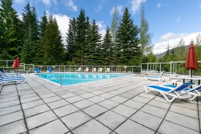a swimming pool with two chairs and a table and two umbrellas at 2BR and Loft in Wildwood Lodge, Mountain Views, Close to Ski Hill, Common Hot Tub, Fireplace, Parking in Whistler