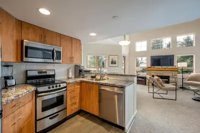 a kitchen with stainless steel appliances and a living room at 2BR plus Loft and Sofabed in Tyndall Stone Lodge, Epic Village Location, Mountain Views, Pool and Hot Tub in Whistler