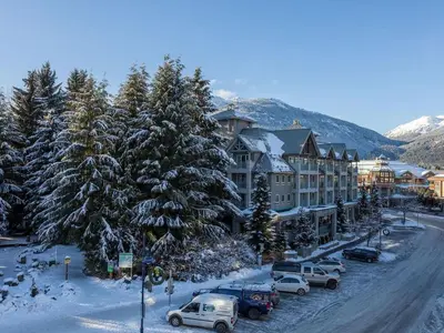 a snowy street with cars parked in front of a lodge at 2BR plus Loft and Sofabed in Tyndall Stone Lodge, Epic Village Location, Mountain Views, Pool and Hot Tub in Whistler