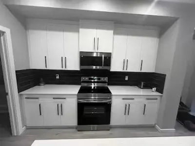a kitchen with white cabinets and a black stove at Brand New Bedroom with private bathroom in Keswick in Edmonton