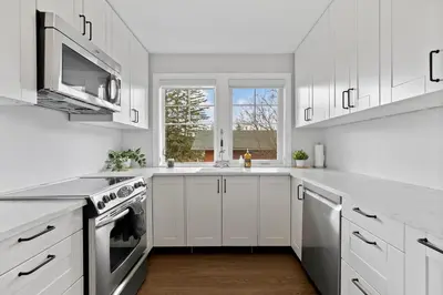a white kitchen with white cabinets and a window at Local Loft - Downtown Okotoks - 2BD - Private in Okotoks