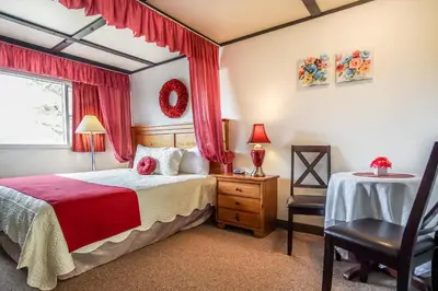 a bedroom with a bed with red curtains and a chair at Gables Motel in Radium Hot Springs