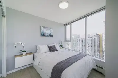 a white bedroom with a bed and a large window at Gorgeous Water View Unit in Downtown Vancouver in Vancouver