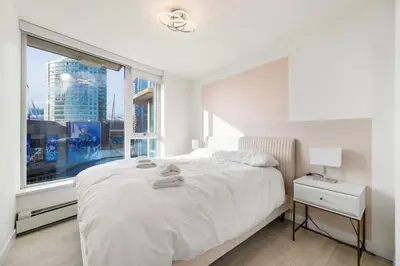 a bedroom with a white bed and a large window at Bright 3BR Downtown Vancouver Condo w Pool & Gym in Vancouver