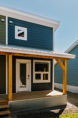 a blue house with a porch and a white door at Trailhead Tuck-Inn in Nordegg