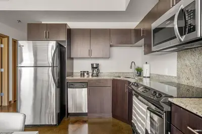 a kitchen with a stainless steel refrigerator and wooden cabinets at The Prime Downtown | Luxe Condo + Free Parking in Calgary