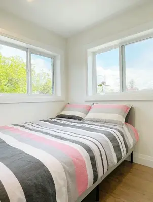 a bed in a white room with two windows at A Beautiful, cozy second floor room for staying in Vancouver